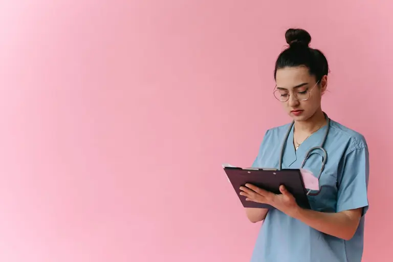 Professional nurse reviewing patient notes on clipboard with pink background, in studio setup.
