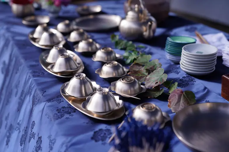 Sleek table setup featuring stainless steel dishes and flatware on a blue tablecloth with leaf decor.