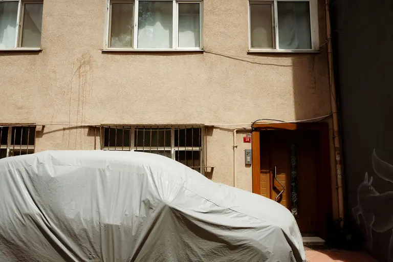 A covered car parked in front of a residential building with barred windows and entrance.